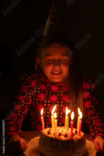 Canvastavla Girl wearing a party hat closing her eyes, making a cherished wish right before blowing out the brightly burning candles on her birthday cake during a dark celebration