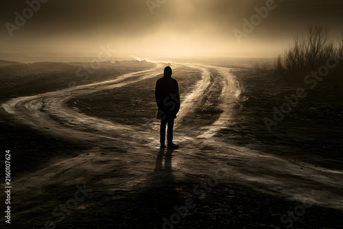 Solitary figure stands at a misty crossroads, bathed in a warm glow, symbolizing choice, uncertainty, and the journey ahead.