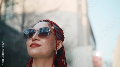 Young woman with red braid putting on sunglasses in city street