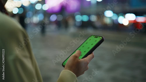 Close up of person holding smartphone with greenscreen while walking in city at night