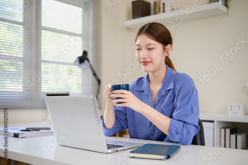 Bild auf Leinwand Young Asian businesswoman checking a smartphone beside her laptop at work