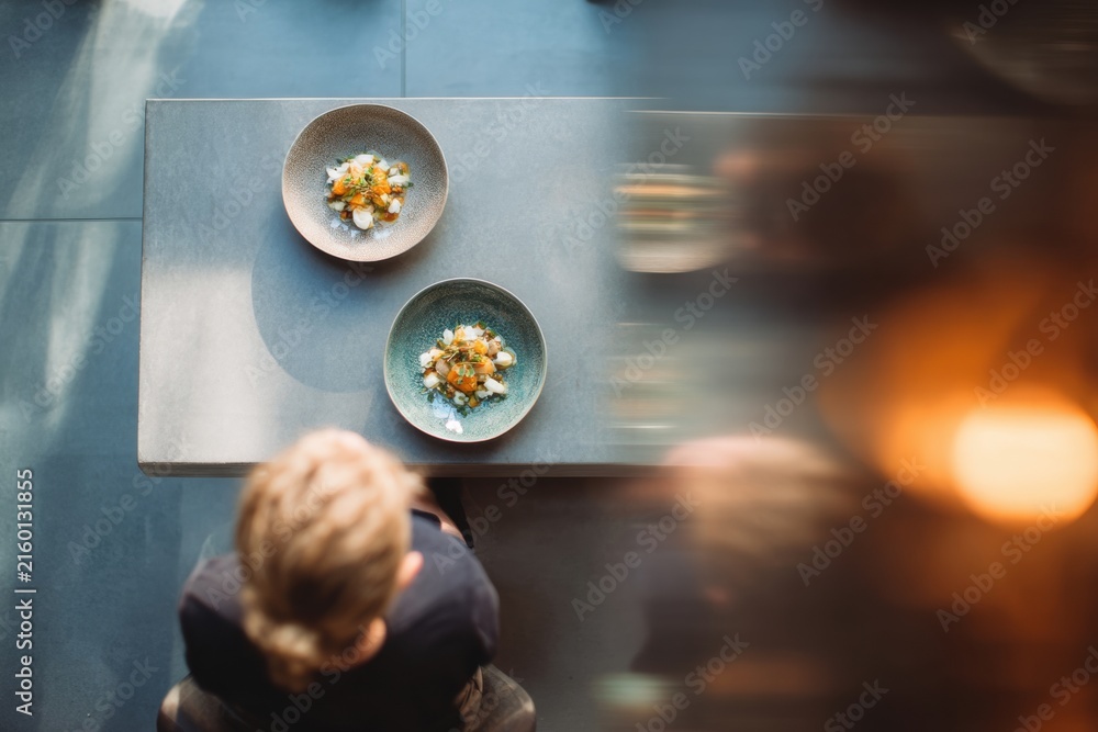 Fototapeta premium Woman sitting at table with gourmet food plates. Overhead view of fine dining experience in modern restaurant. Culinary art and gastronomy concept for luxury lifestyle advertisement.