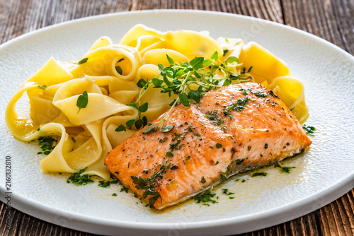 Pasta with baked salmon steak on wooden table
