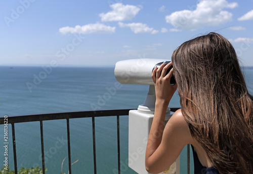 Young woman observing distant ocean view with coin operated telescope