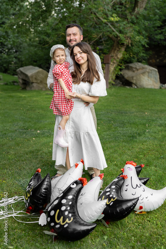 Konstfotografi Happy family portrait outdoors surrounded by colorful chicken balloons on grass
