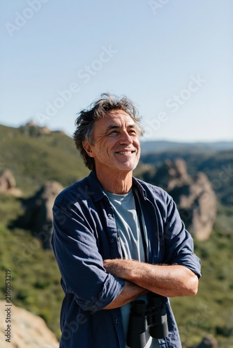 Portrait of a middle aged man with binoculars on a sunny hillside for adventure travel background and outdoor banner design