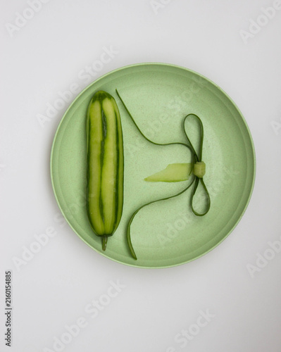Top view of peeled green cucumber and cucumber peel in the form of a bow pattern on a flat plate. Cleaning and cutting vegetables.