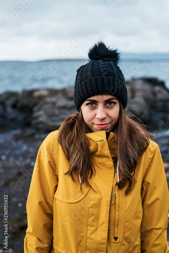 White Woman in yellow jacket and black hat on rocky beach in a beach