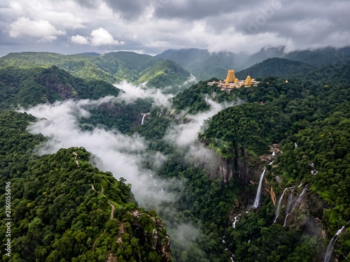 Breathtaking aerial view of winding ghat roads on lush green misty mountains leading to a sacred temple, hyper-realistic digital landscape