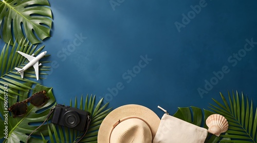 Flat lay composition of tropical vacation accessories on a dark blue background.