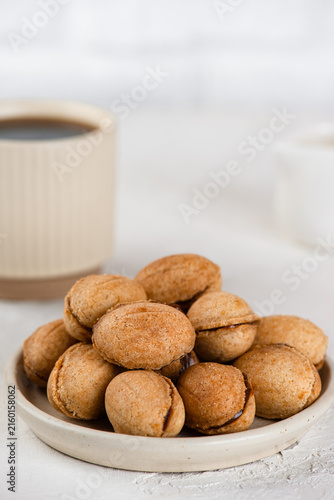 Sugar free vegan cookies filled with boiled coconut condensed milk served on ceramic plate with coffee. Vertical orientation.