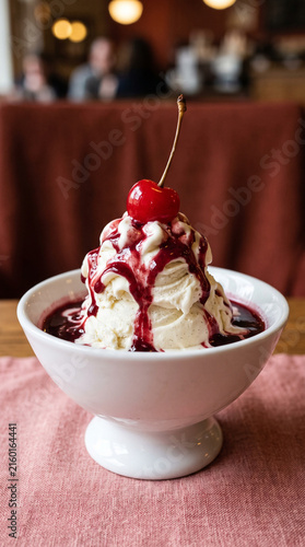 Classic vanilla ice cream sundae topped with berry syrup and maraschino cherry in dessert bowl