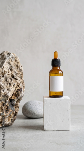 Amber glass dropper bottle mockup on white stone cube pedestal with natural stones