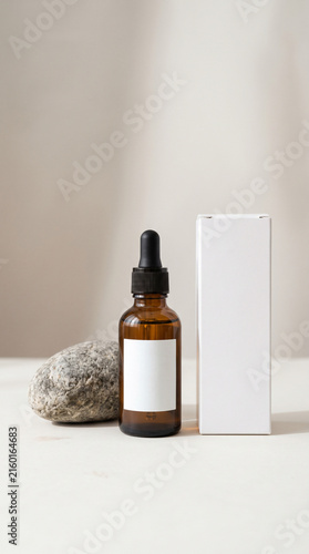 Amber glass dropper bottle and white box packaging mockup with natural stone on neutral background