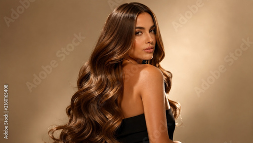 Beautiful woman with long wavy brown hair posing over shoulder