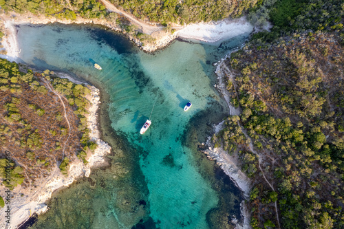 Aerial view of Cala di Malfalcu featuring turquoise waters, anchored boats, and lush Mediterranean vegetation in Santo-Pietro-di-Tenda, Corsica, France.
