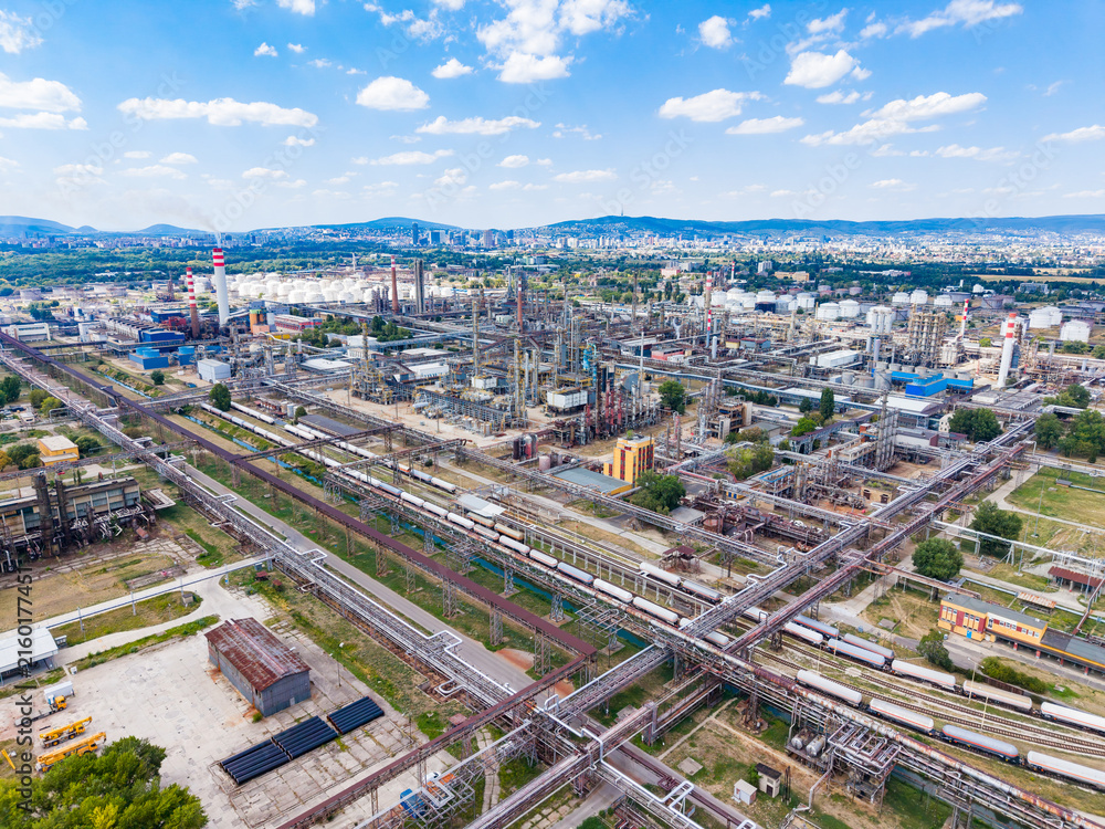 Fototapeta premium Large industrial area with factories, tanks, and train tracks in a city setting under a blue sky