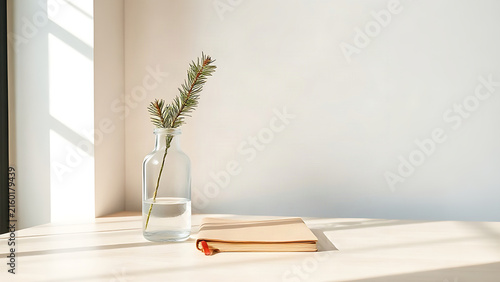 Pine branch in glass bottle vase on wooden desk next to blank notebook, simple workspace and nature concept