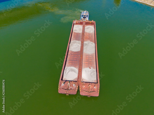 Принти на полотні Cargo barge is floating on green water while workers prepare for unloading near