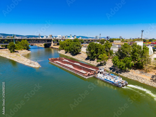 Barge moves along the river with city skyline in background and a bridge over the water