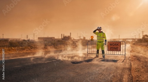 Tired road construction worker wiping sweat from forehead near work zone sign on hot steaming asphalt road during extreme heatwave concept.