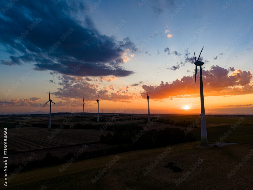 Obraz premium Wind turbines stand tall as the sun sets over the horizon, casting a warm glow across the landscape in a rural setting