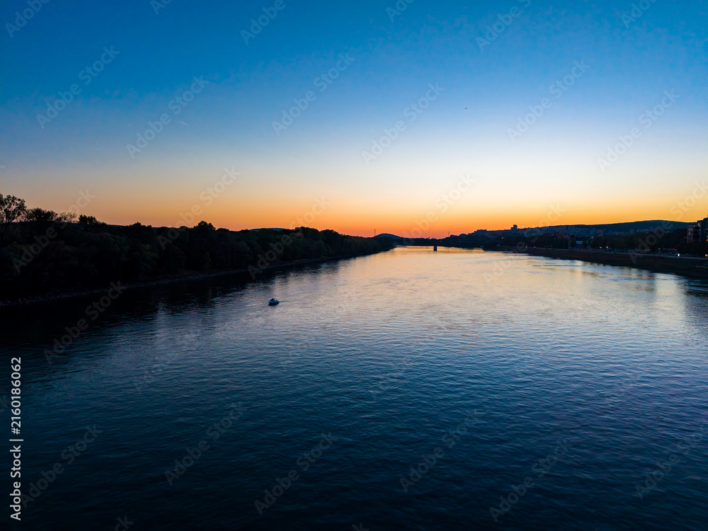 Fototapeta premium River during sunset seen from a bridge with clear skies and some land along the banks in a quiet location