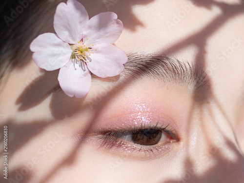 Macro beauty shot of female eye with soft pastel pink glitter eyeshadow and cherry blossom in sunlight