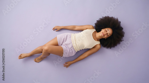 Top view of woman with afro hair lying on her back with eyes closed on a purple background