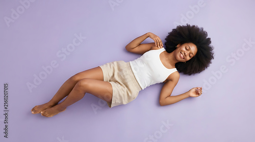Top view of woman with afro hair lying on her back smiling on a purple background