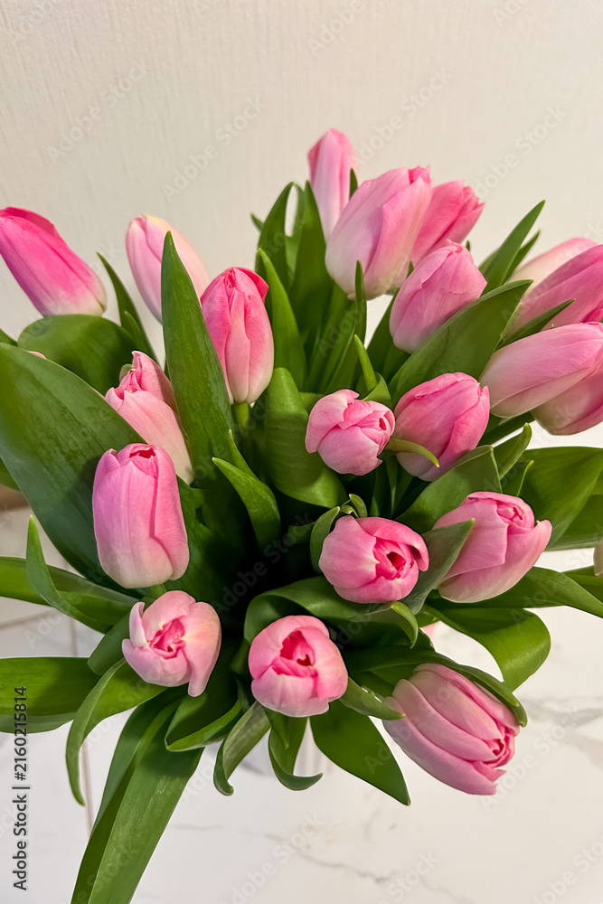 Fototapeta premium Bouquet of pink tulips arranged on a table with green leaves