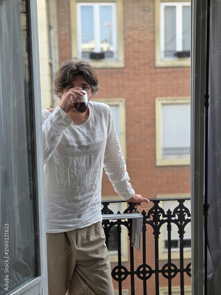 Fototapeta premium Man in a white linen shirt drinking coffee on a balcony on a calm summer morning