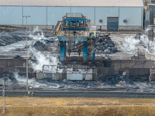 Aerial view of the Tata Steel industrial facility featuring heavy machinery processing molten metal with rising steam and slag piles in Velsen-Noord, Noord-Holland, Netherlands.