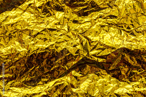 Abstract crumpled gold foil with a reflective metallic texture, creating a luxurious golden background for design, packaging, advertising and creative projects.