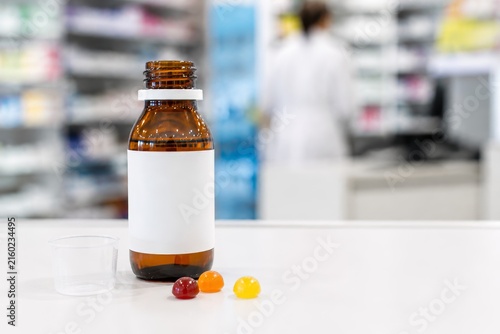 Frasco de medicina sobre un mostrador en una farmacia con un trabajador al fondo