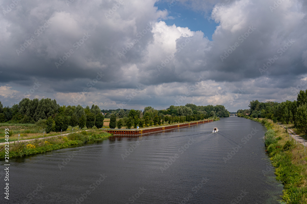 Fototapeta premium Wide view of canal shipping route with steel sheet pile wall along bank under cloudy sky in Brandenburg Germany with copy space