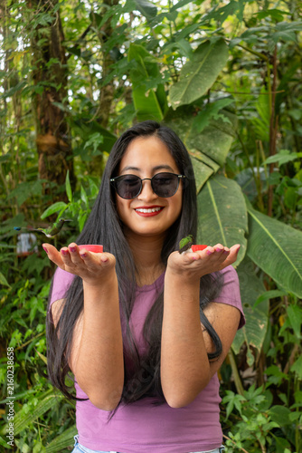 Young woman enjoying a unique ecotourism experience, smiling happily while feeding colorful hummingbirds directly from her hands in the lush mindo cloud forest
