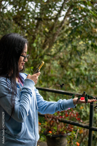Woman in mindo. Ecuador. Smiling while feeding several vibrant hummingbirds from her hand