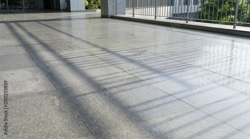 Monochromatic polished stone tiles showing soft linear silhouettes cast by an outdoor safety barrier on a bright afternoon floor ceramic gray tile shadow fence background backdrop texture stone