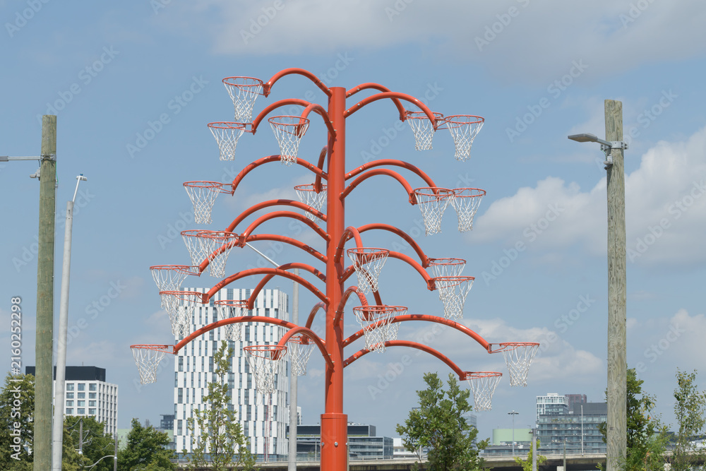 Fototapeta premium view of Alexandre Arrechea's Orange Functional, 2022, composed of steel and basketball nets, #1, in the plaza of Old Firehall 30, at Biidaasige Park, Port Lands, Toronto