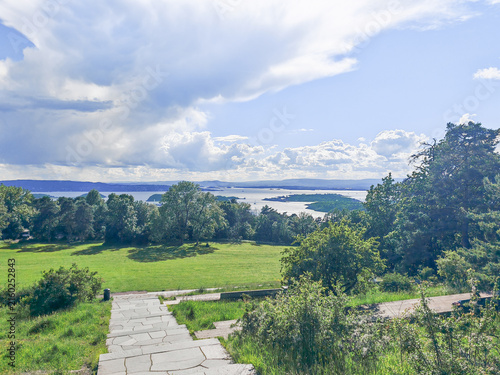 Scenic dirt path leading to panoramic view of Oslo fjord with lush greenery and distant cityscape