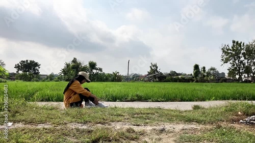 Slow motion video of a young Muslim woman in a hijab standing up and limping after suffering a sprained ankle. She walks with difficulty on a path next to a green rice field. Sports concept.