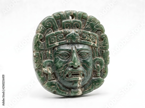 Hand carved mayan jade pendant with intricate facial details sits on a white surface