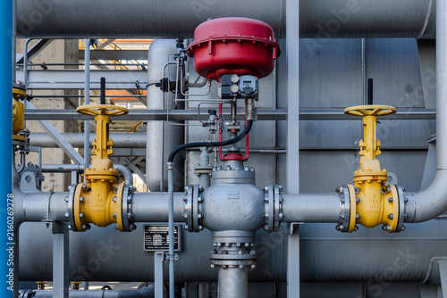 Фотография Close-up of yellow gate valves and a red actuator control valve installed on gray steel pipelines with flanges and instrumentation at a petrochemical industrial plant