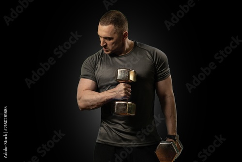 Принти на полотні Focused, athletic male athlete lifts a dumbbell for bicep curl training inside a dark studio