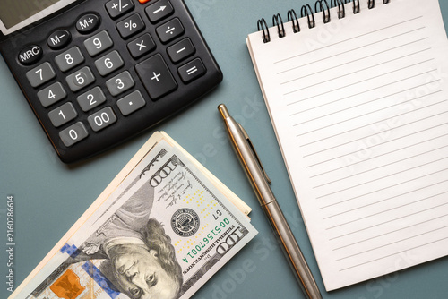 US dollar banknotes with calculator, pen and blank lined notebook arranged on a desk, representing budgeting, accounting, expenses and financial planning.