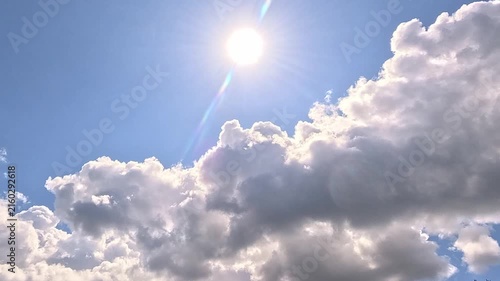 A bright sun shines in a blue sky as large white cumulus clouds drift and shift steadily across the frame, gradually changing shape and position throughout the entire scene.