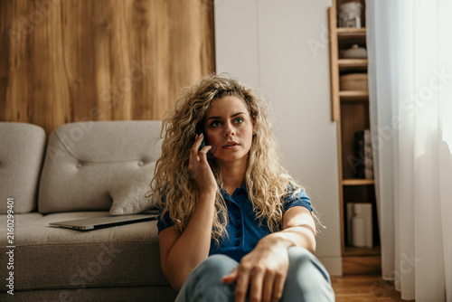 Woman having concerned phone call sitting on floor