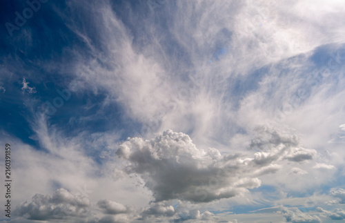 Vibrant blue sky displaying a mix of atmospheric layers, featuring delicate, feathered high-altitude cirrus clouds contrasting with a distinct, puffy white cumulus cloud formation in the lower section