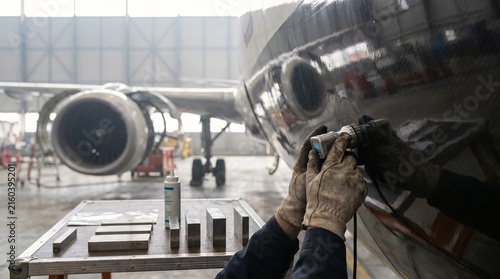 Technician hands inspecting composite aircraft wing and fuselage in industrial hangar